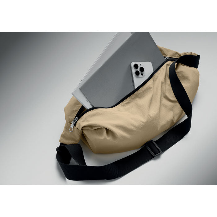 SLING - Bolsa urbana cruzada de nailon color beige con computadora y teléfono dentro sobre fondo gris.