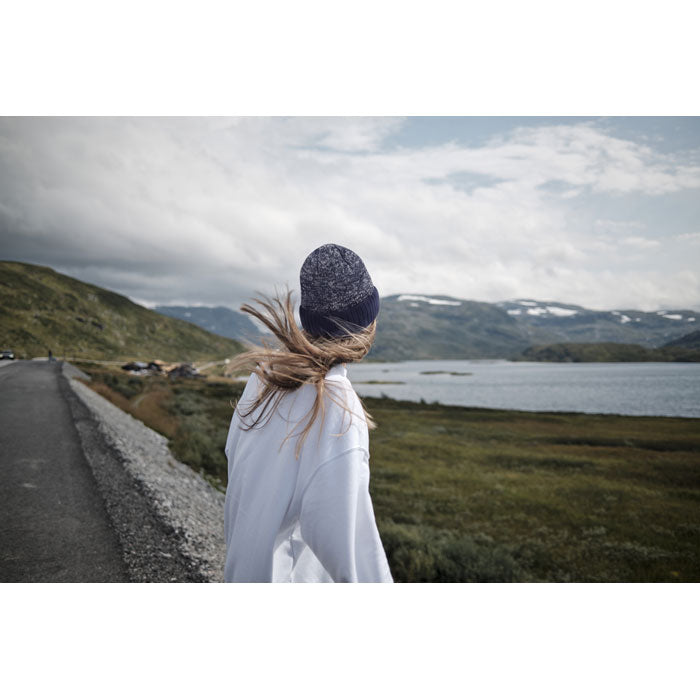 PUNTOS - Gorro de punto con dobladillo en un paisaje montañoso, mujer con cabello largo y suelto, vistiendo abrigo blanco.