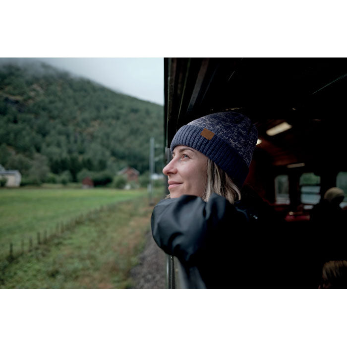 Mujer usando PUNTOS - Gorro de punto con dobladillo mientras mira por la ventana de un tren en un paisaje montañoso.
