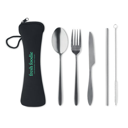 Cuchara, tenedor, cuchillo, pajita plateados y cepillo alineados junto a la funda.  