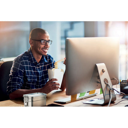 Hombre comiendo frente a un ordenador sobre una mesa con una fiambrera de metal