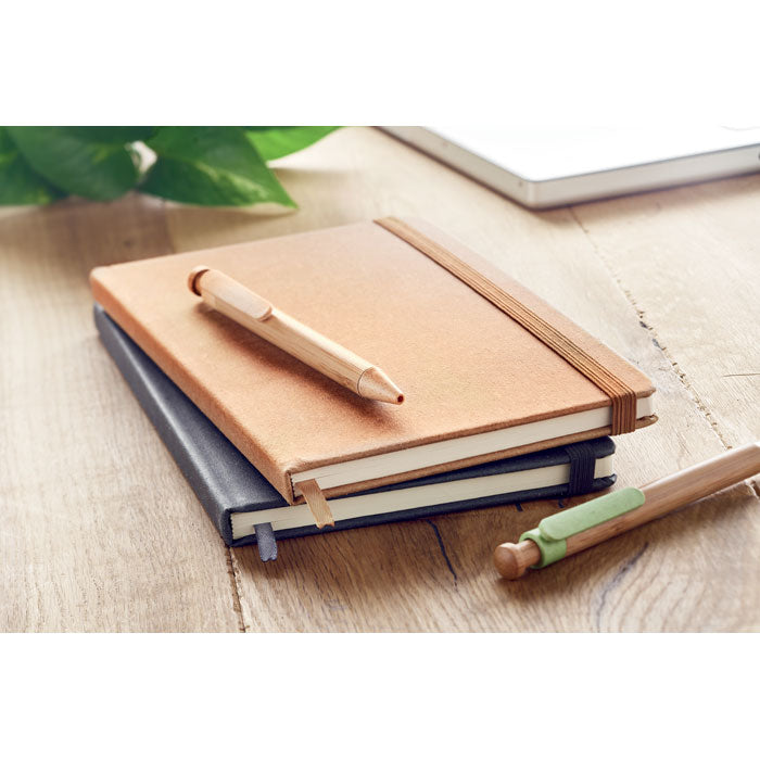 Libretas A5 en tonos marrón y negro, con bolígrafo de madera y detalles ecológicos sobre una mesa de madera.