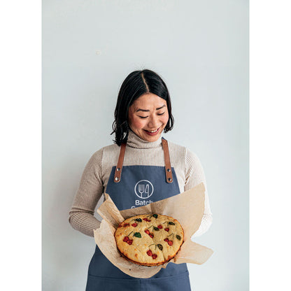 Chica con pastel en la mano y con delantal azul marino personalizado en el peto con un logotipo
