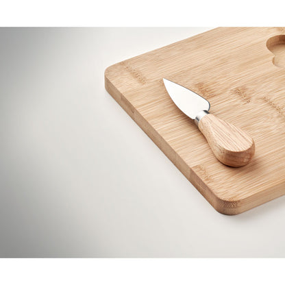 Detalle de cuchillo de queso sobre tabla de cortar de madera con fondo gris