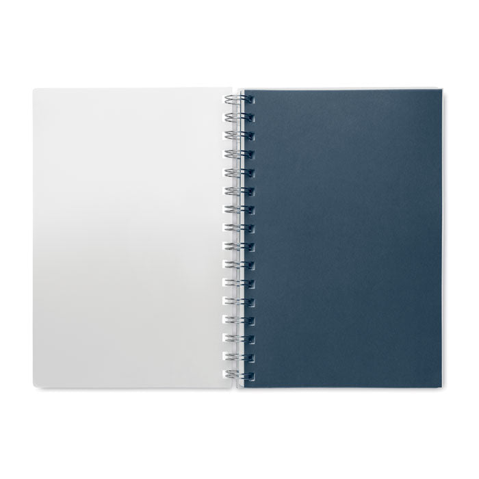 Interior de libreta A5 con tapa de RPET, mostrando páginas blancas y azules, encuadernación espiral.