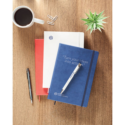 Libreta roja, blanca y azul de cierre goma sobre mesa de madera con bolígrafos y taza de café