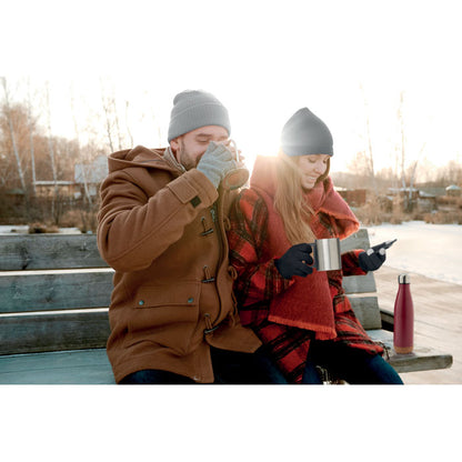 Pareja en paisaje invernal bebiendo en tazas metálicas