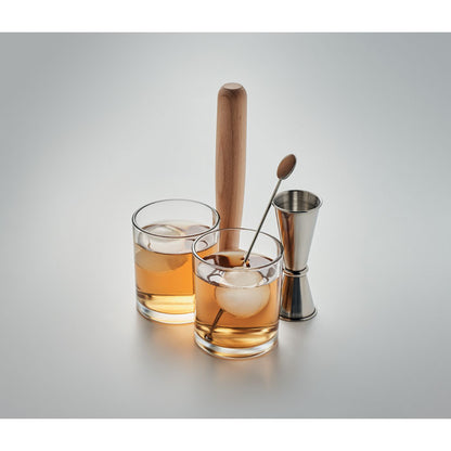 Coctel en vaso de cristal con accesorios para su preparación sobre un fondo gris neutro