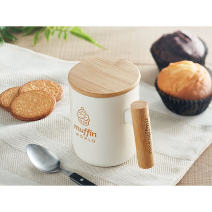 Taza de porcelana blanca con asa y tapa de bambú personalizada con un logotipo en una mesa de desayuno