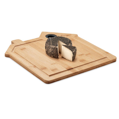 Trozo de queso sobre tabla para cortar en bambú con forma decorativa de casa.