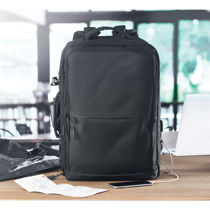 Mochila para portátil sobre mesa de oficina con móvil cargando a través del USB lateral de la mochila