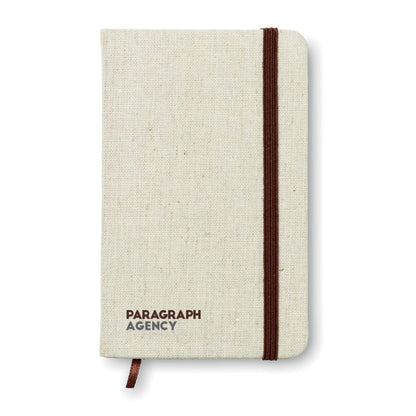 Libreta con tapa de tela canvas color crudo y goma y marcapáginas marrón personalizada con logotipo en parte inferior izquierda
