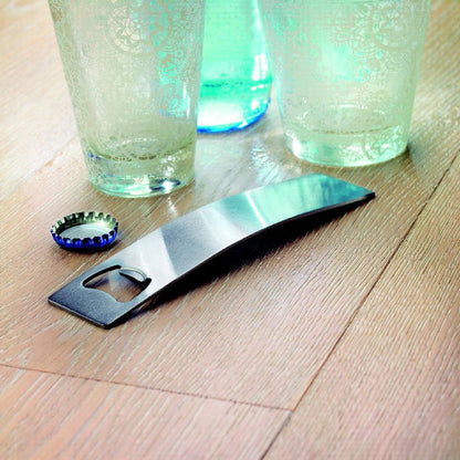 Abrebotellas metálico sobre una mesa de madera con vasos alrededor