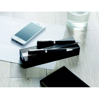 Bolígrafo y roller negro sobre caja de presentación en mesa de madera sobre unos folios