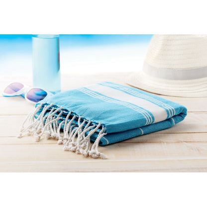 Toalla doblada tuquesa con rayas blancas y flecos en mesa de madera en la playa