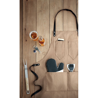 Delantal color arena sobre una superficie de madera con accesorios de cocina dentro de los bolsillos