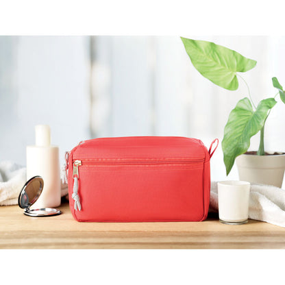 Neceser rojo sobre mesa de madera con un espejo y un vela al lado