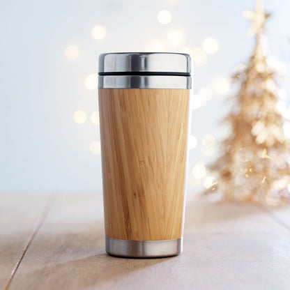 Vaso de acero inoxidable con revestimiento de bambú sobre mesa de madera y con un árbol de navidad en segundo plano