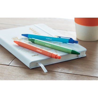 3 bolígrafos: azul, naranja y verde sobre libreta blanca en mesa