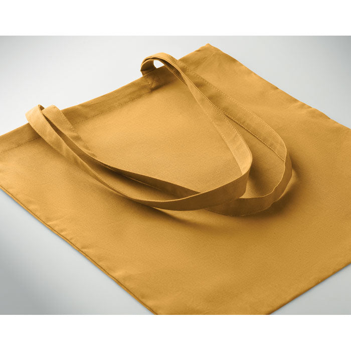 Bolsa de algodón en color mostaza, con asas largas y diseño simple para uso cotidiano.