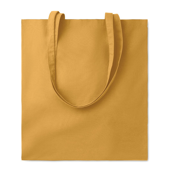 Bolsa de algodón color ocre con asas largas, textura lisa y dimensiones amplias.
