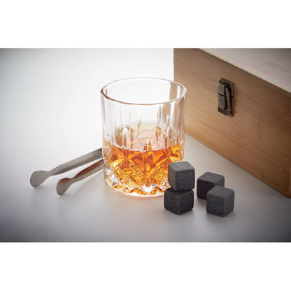 Vaso con whisky al lado de cubitos de piedra, pinzas y caja de madera