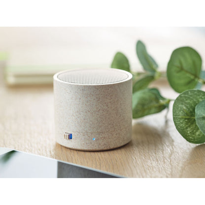 Altavoz redondo de paja de trigo con interruptor e indicador luminoso sobre mesa de madera