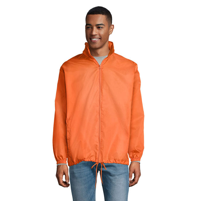 Hombre usando una chaqueta cortaviento naranja, parte de SHIFT - SHIFT CORTAVIENTO UNIX, con cremallera y cordones ajustables.