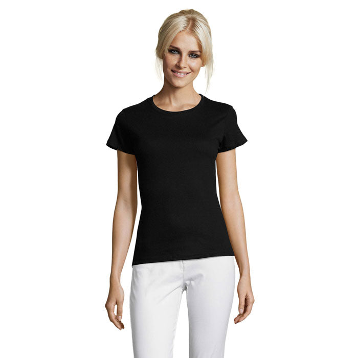 Mujer sonriente vistiendo camiseta negra de cuello redondo, ajuste ceñido y mangas cortas, con pantalones blancos.