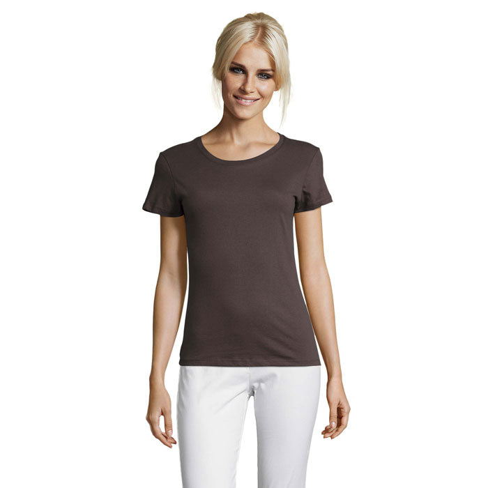 Mujer sonriendo con camiseta de color marrón de cuello redondo, ajuste ceñido y mangas cortas, combinada con pantalones blancos.