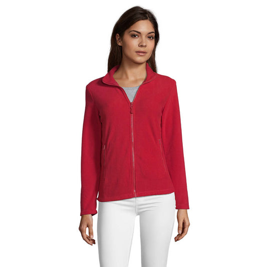 Chaqueta roja de poliéster con cremallera y cuello alto, ideal para el uso diario. Vista frontal de la modelo con pantalones blancos.