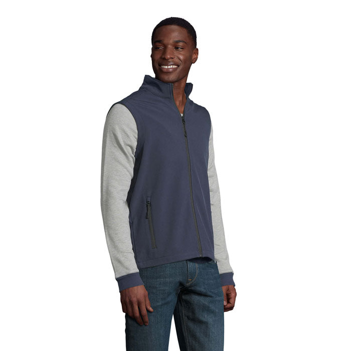 Vista lateral de chaleco softshell en tonalidades gris y azul para hombre, con cremallera y bolsillos.
