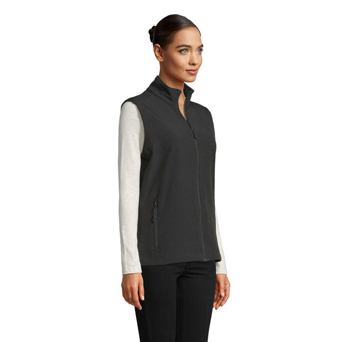 Vista lateral de chaleco softshell negro para mujer, con cremallera y dos bolsillos, ideal para actividades al aire libre.