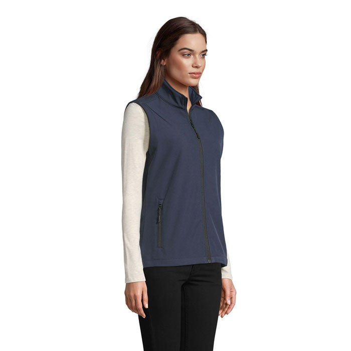 Vista lateral de chaleco softshell azul para mujer, con cremallera y dos bolsillos, ideal para uso diario.