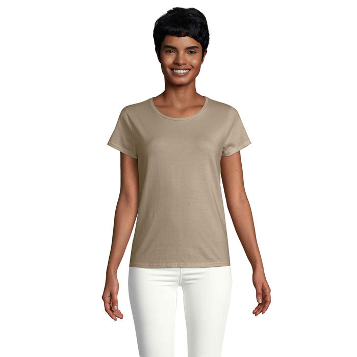 Modelo femenina sonriente vistiendo una camiseta ajustada en color beige de algodón orgánico, con cuello redondo.