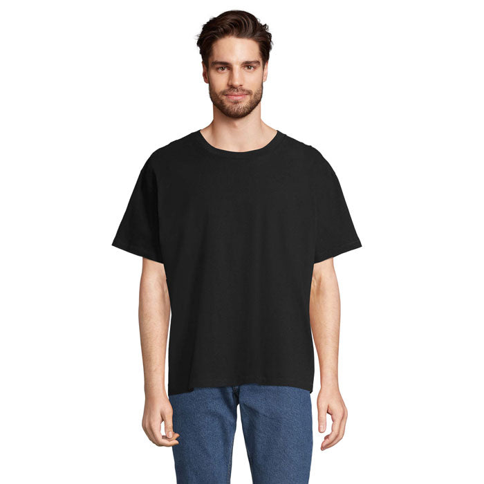 Modelo masculino vistiendo una camiseta oversize negra, confeccionada en algodón reciclado, con corte de hombro caído.