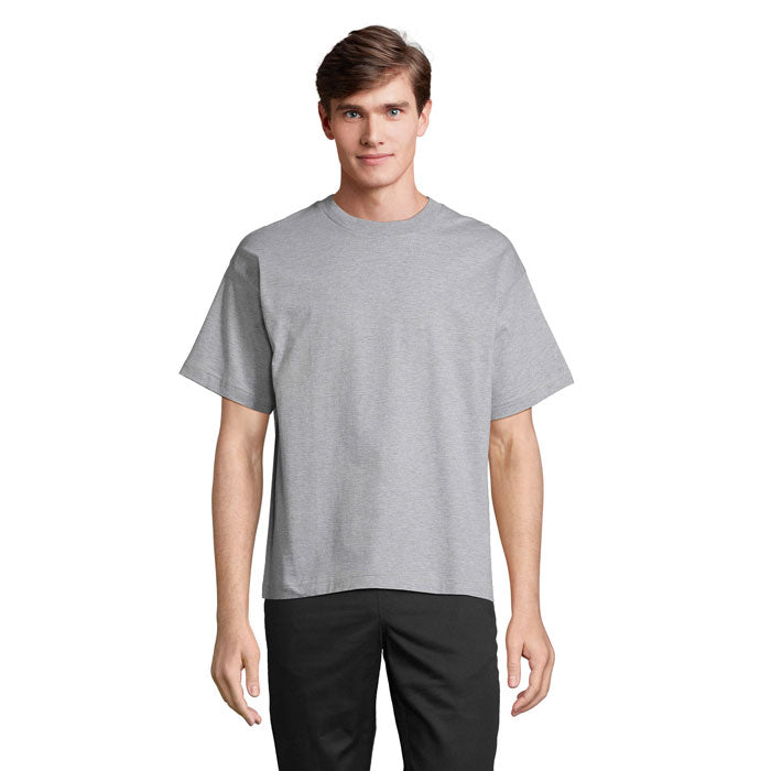 Modelo masculino luciendo una camiseta oversize gris de algodón reciclado, con cuello redondo y corte moderno.
