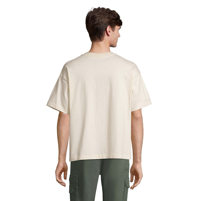 Vista trasera de camiseta oversize en color crema, con corte cómodo y de hombro caído, combinada con pantalones verdes.