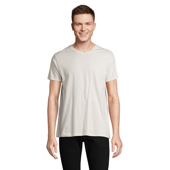 Modelo masculino sonriendo con camiseta de cuello en V color blanco roto, 100% algodón, corte moderno, vista frontal.