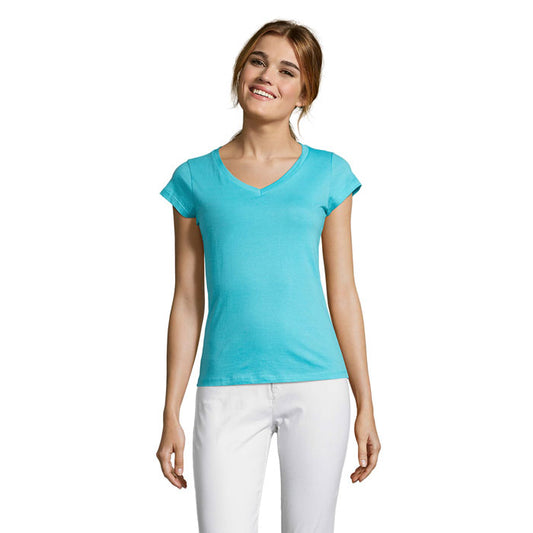 Mujer sonriente vistiendo camiseta azul clara con escote en pico y manga corta, frente a un fondo neutro.