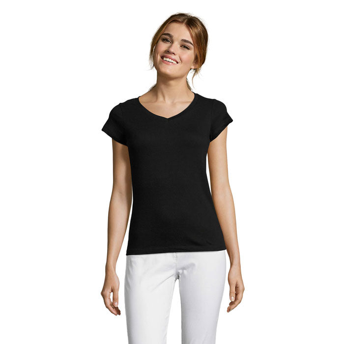 Mujer sonriente luciendo una camiseta negra con escote de pico y manga corta, combinada con pantalones blancos.