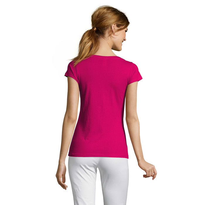 Vista trasera de una camiseta fucsia para mujer, 100% algodón y corte ajustado, combinada con pantalones blancos.